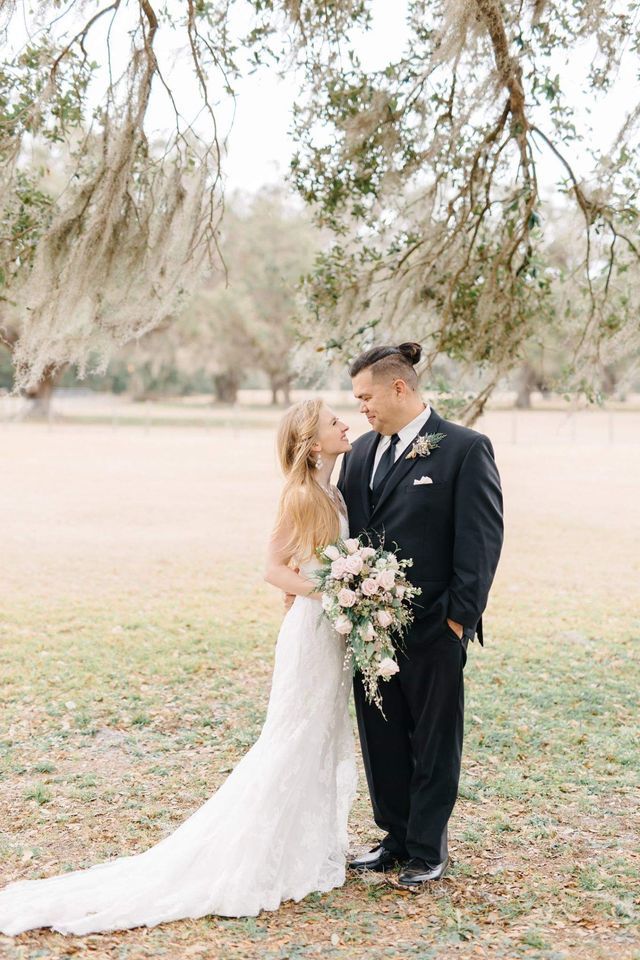 A bride and groom are standing under a tree in a field.