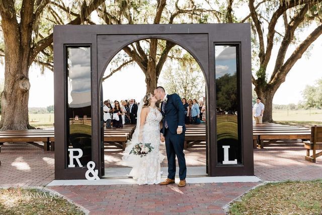 A bride and groom kissing in front of a wooden arch with their initials on it.