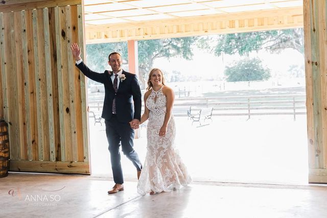 A bride and groom are walking through a barn holding hands.