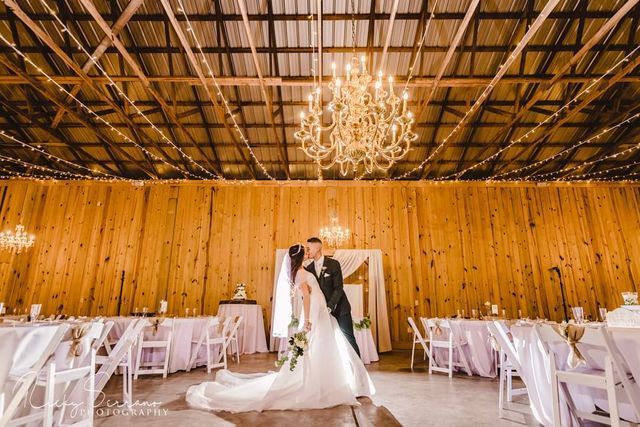 A bride and groom are kissing in a barn at their wedding reception.