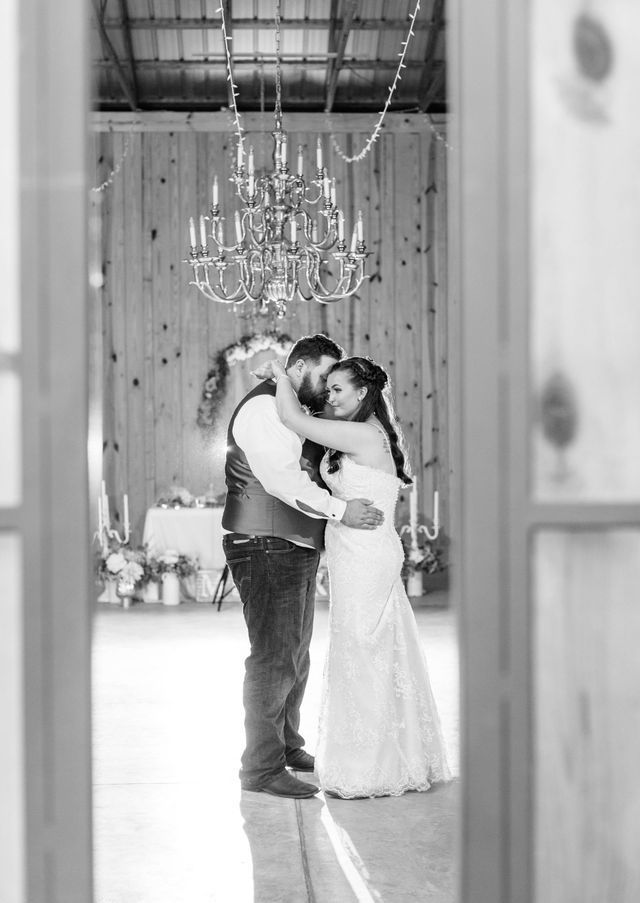 A black and white photo of a bride and groom dancing in a barn.