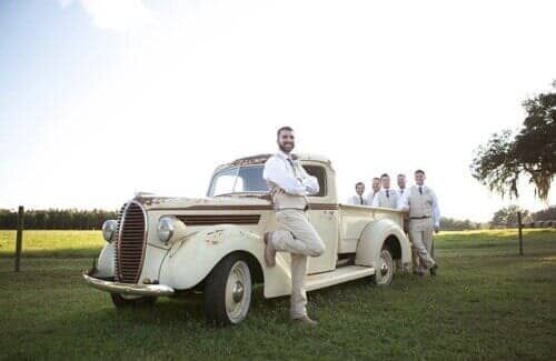 The groom and his groomsmen are posing for a picture in front of an old truck.