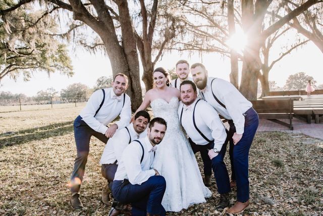 A bride and her groomsmen are posing for a picture in front of a tree.