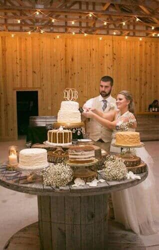 A bride and groom are cutting their wedding cake on a wooden table.