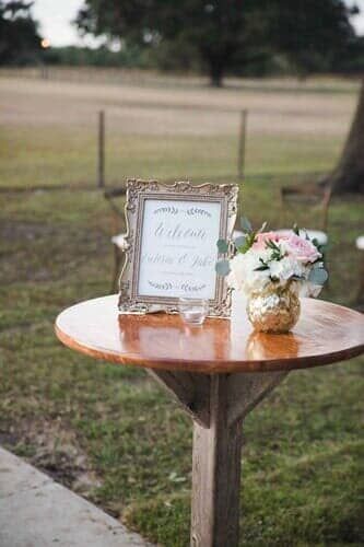 A wooden table with a sign and a vase of flowers on it.
