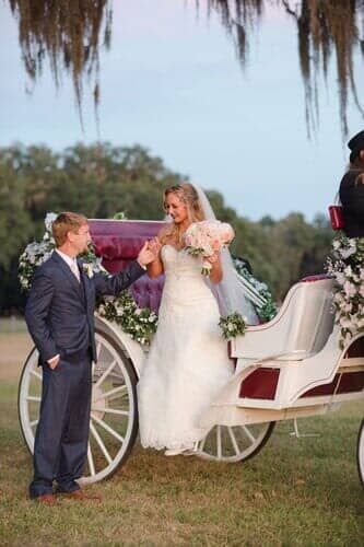 A bride and groom are standing next to a horse drawn carriage.