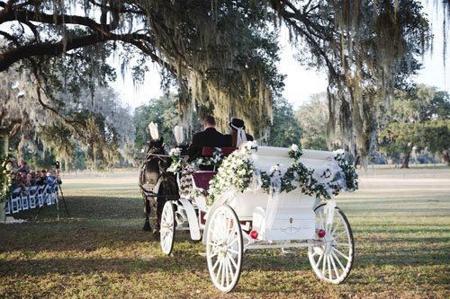 A bride and groom are riding in a horse drawn carriage.