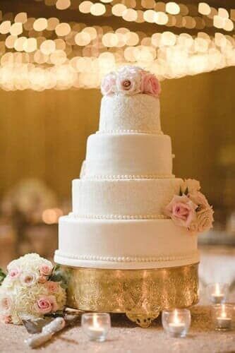 A wedding cake is sitting on top of a gold cake stand on a table.