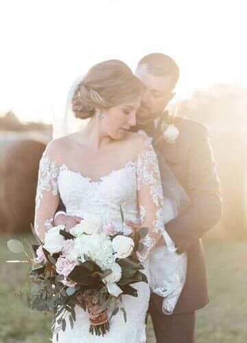 A bride and groom are posing for a picture in a field with hay bales in the background.