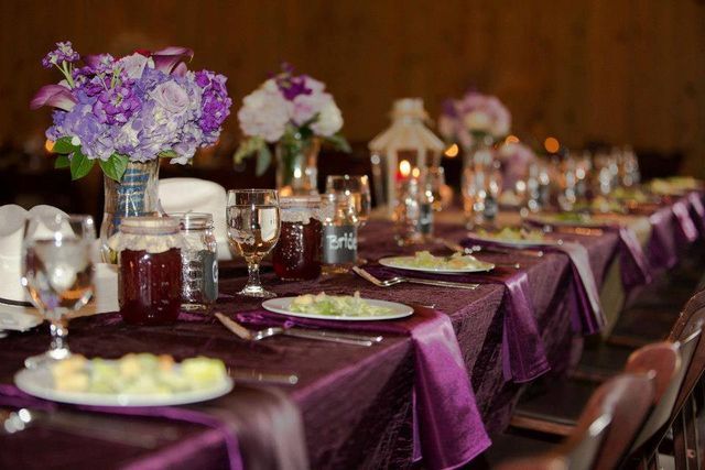 A long table set for a wedding reception with purple napkins and plates.