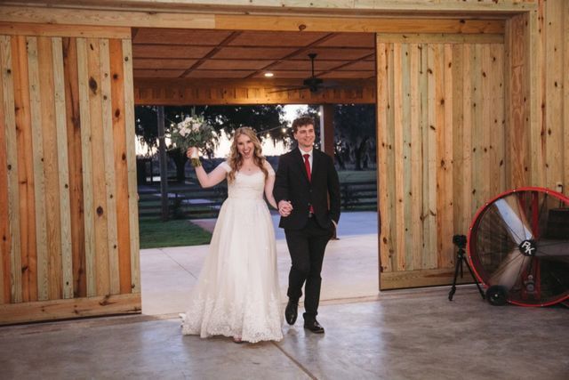 A bride and groom are walking through a wooden building holding hands.
