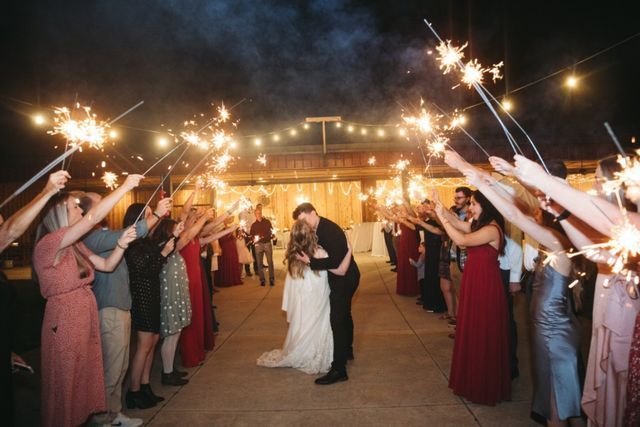 A bride and groom kissing in front of a crowd of people holding sparklers.