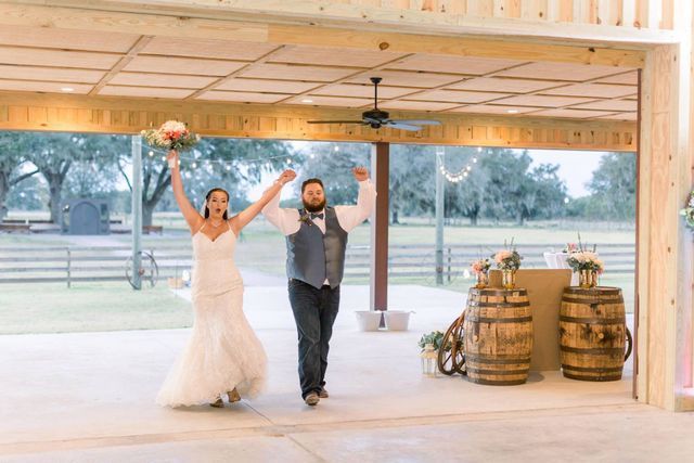 A bride and groom are walking in a room with their arms in the air.