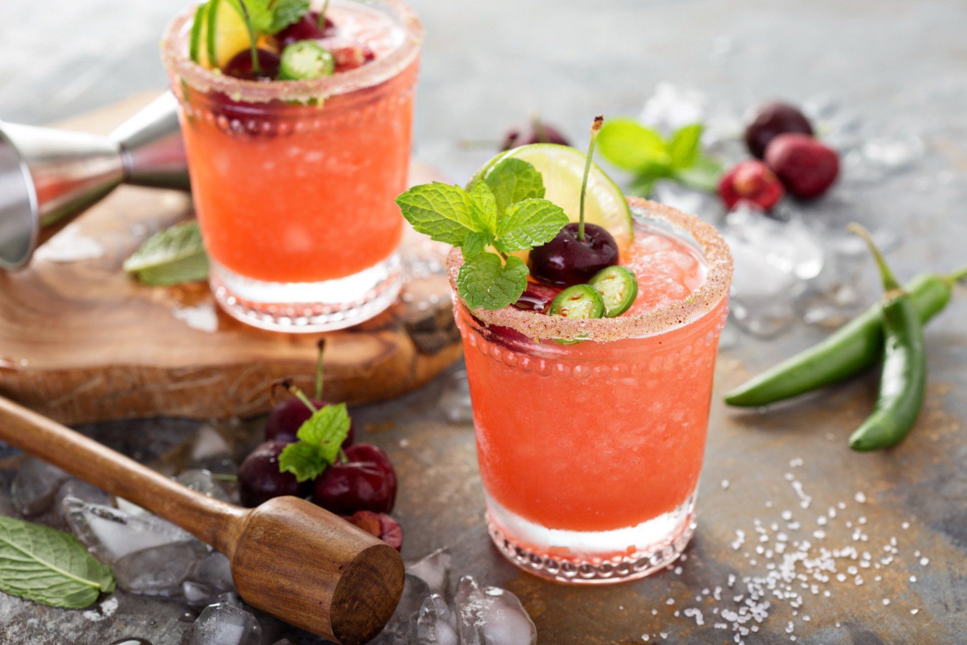 Two glasses of red liquid with cherries and limes on a table.