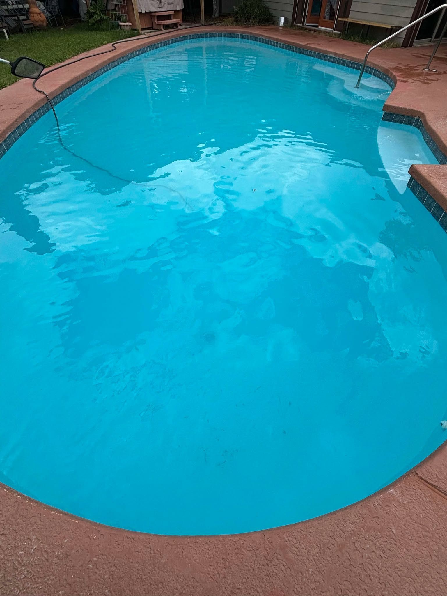 A turquoise backyard swimming pool with a stone patio edge and a metal entry railing.