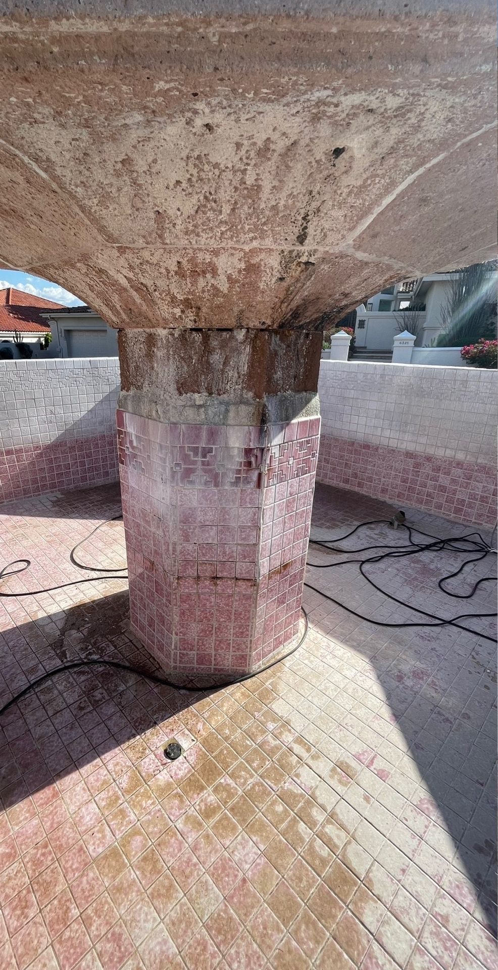A weathered, octagonal fountain pedestal with pink-toned stone tiles standing in an empty, tiled pool.