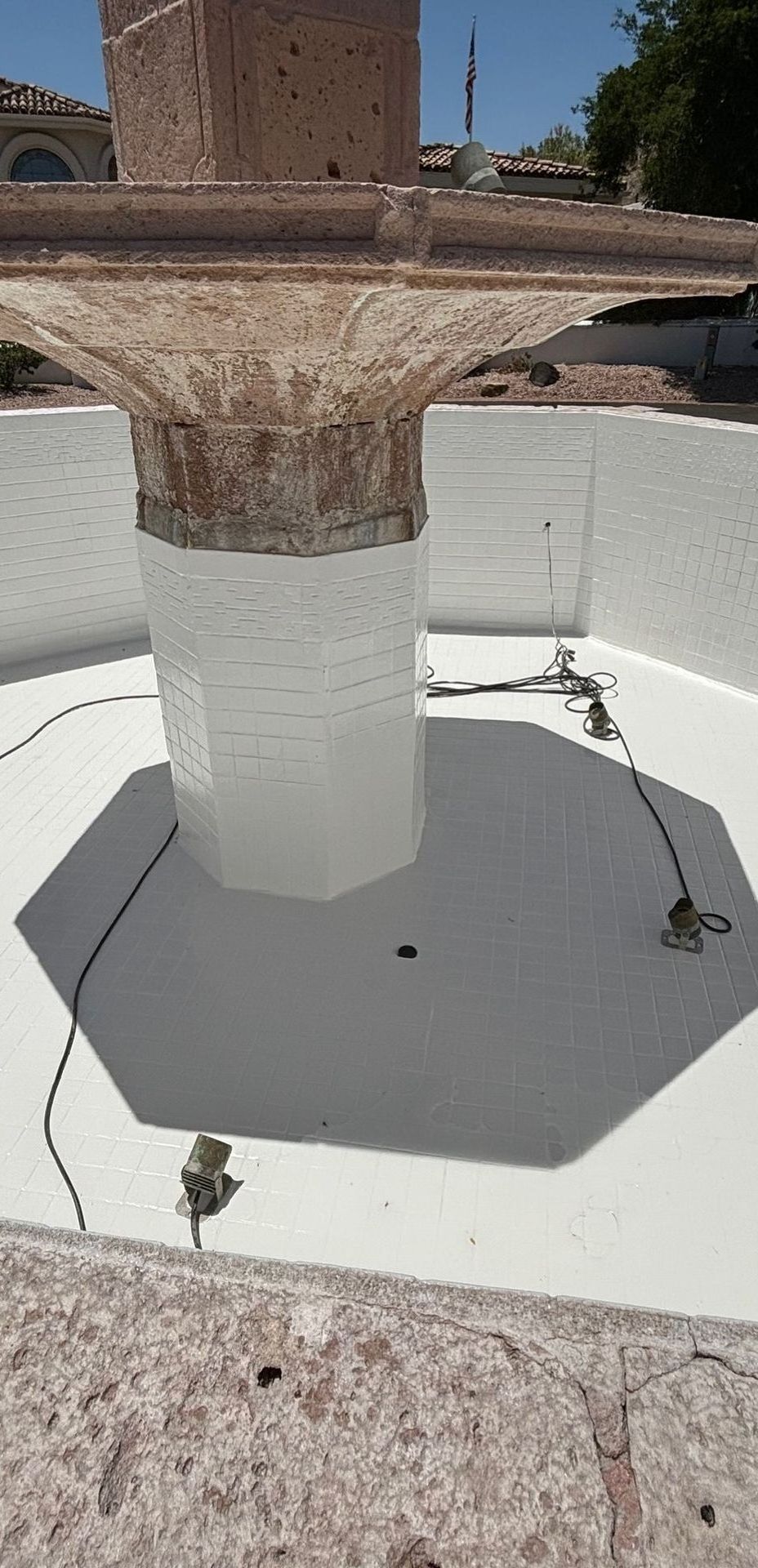 A tiered stone fountain base with white-painted walls and floor, featuring installed lighting fixtures in an outdoor area.