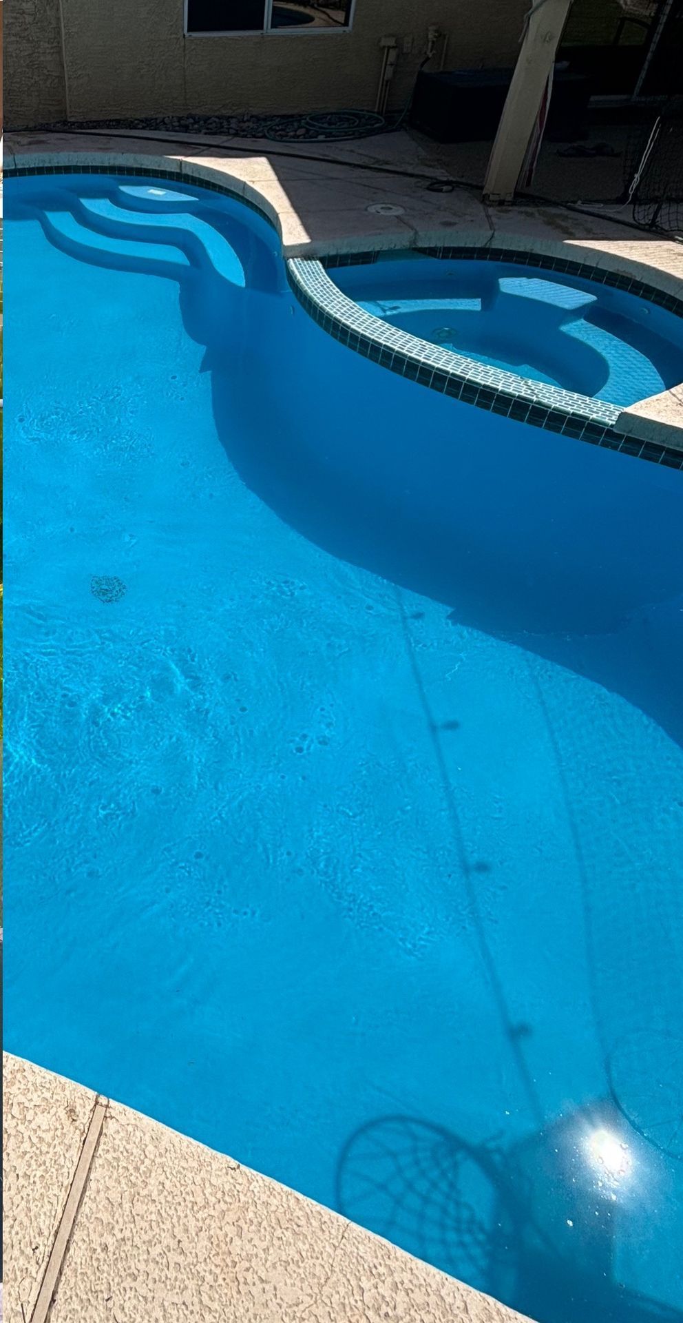 A bright blue kidney-shaped swimming pool with a connected circular spa and tiered entry steps.