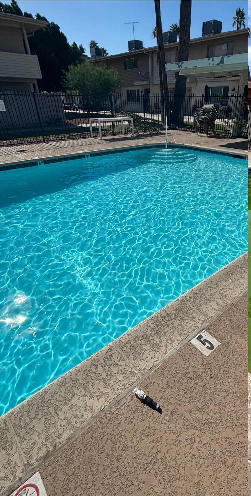 A bright blue swimming pool sits at an apartment complex, with depth markers visible on the concrete deck.