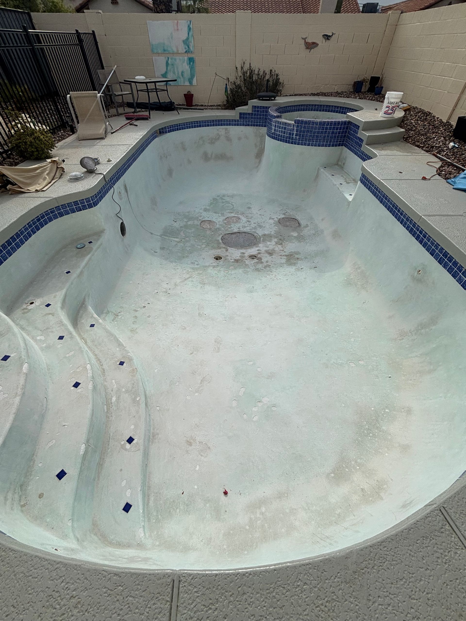 Empty drained swimming pool with chipped blue tile edging and debris around the deck