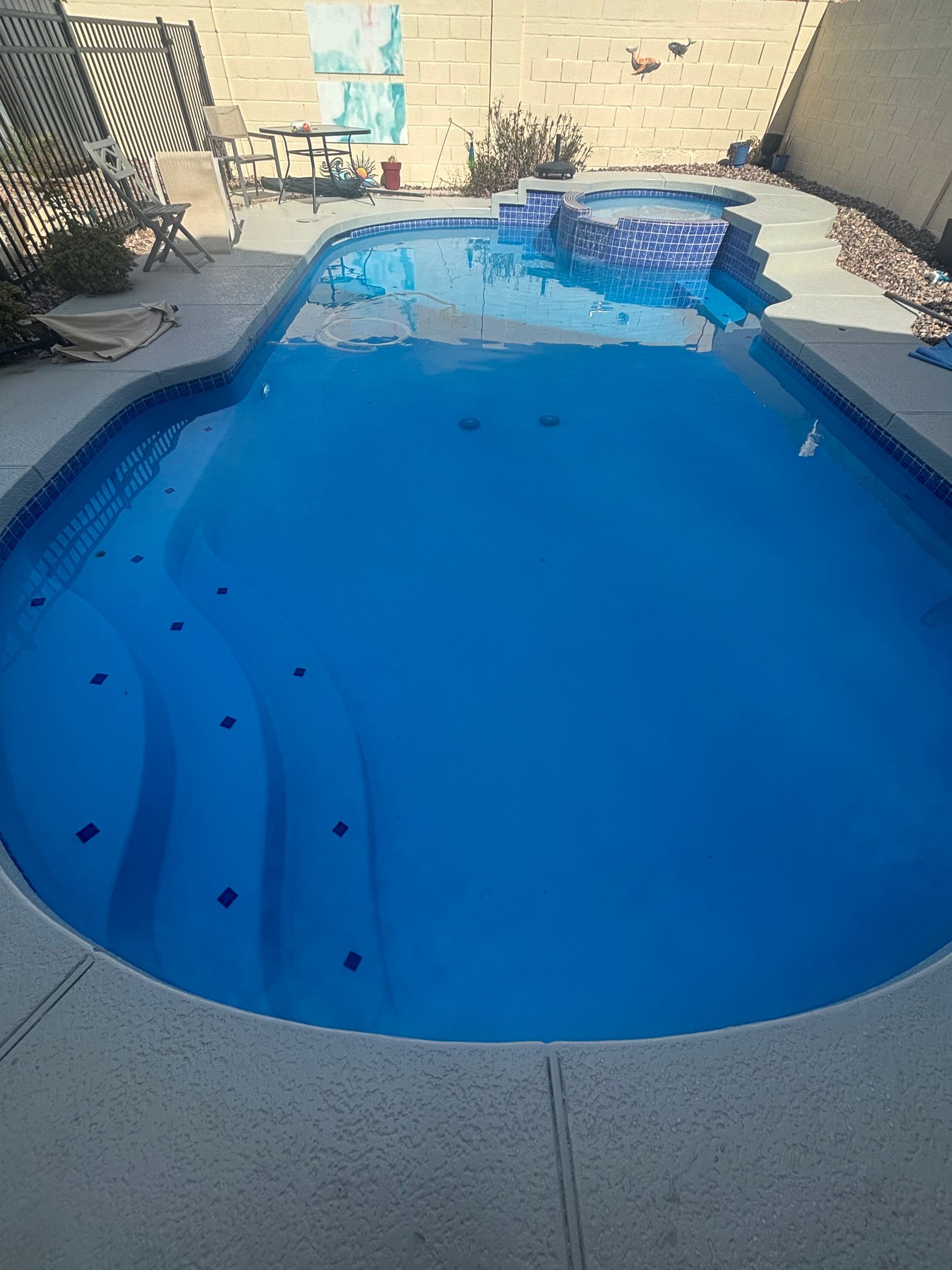Backyard swimming pool with bright blue water and concrete deck, viewed from the shallow end