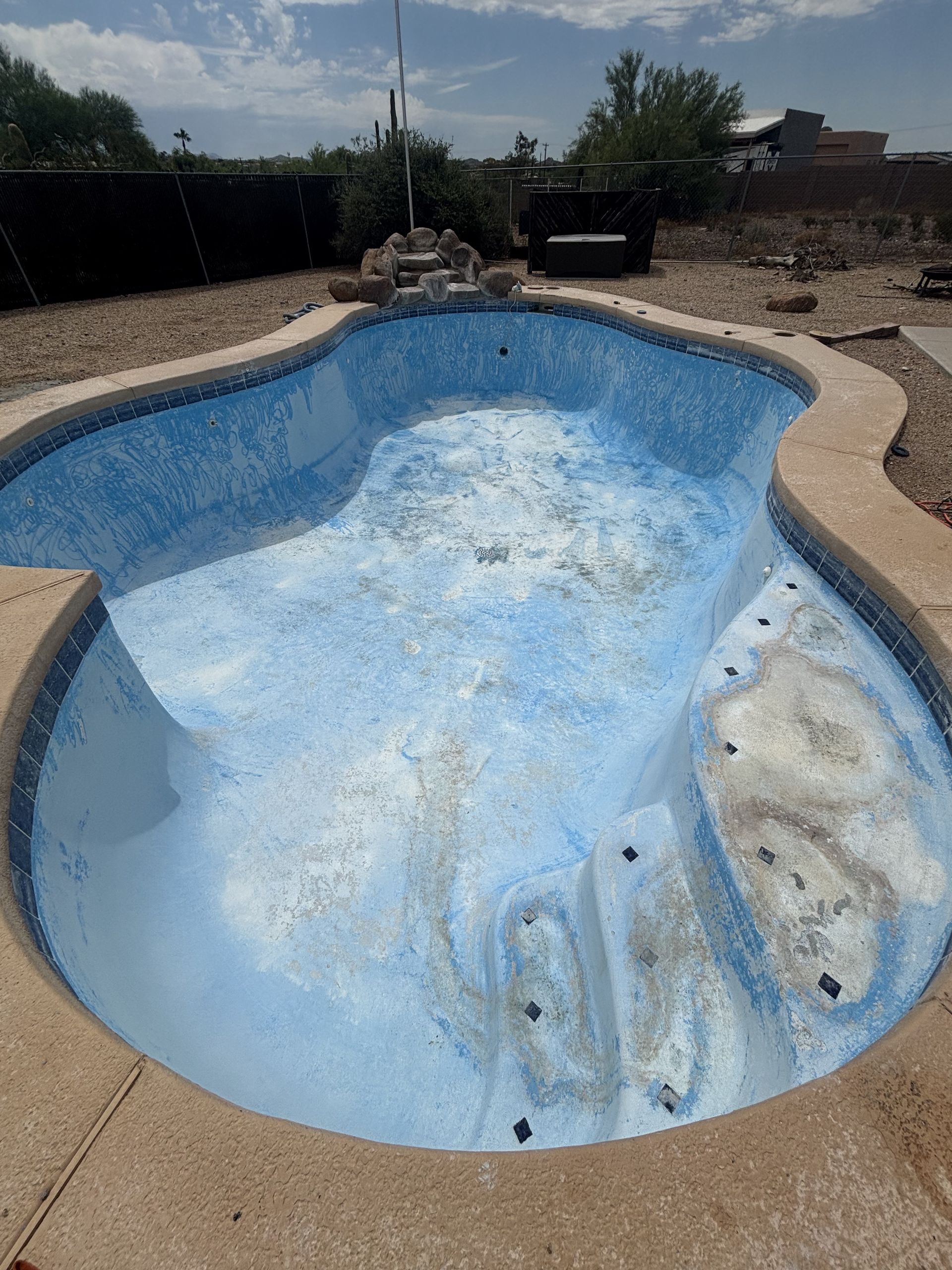 Empty backyard swimming pool with peeling blue interior under bright sunlight