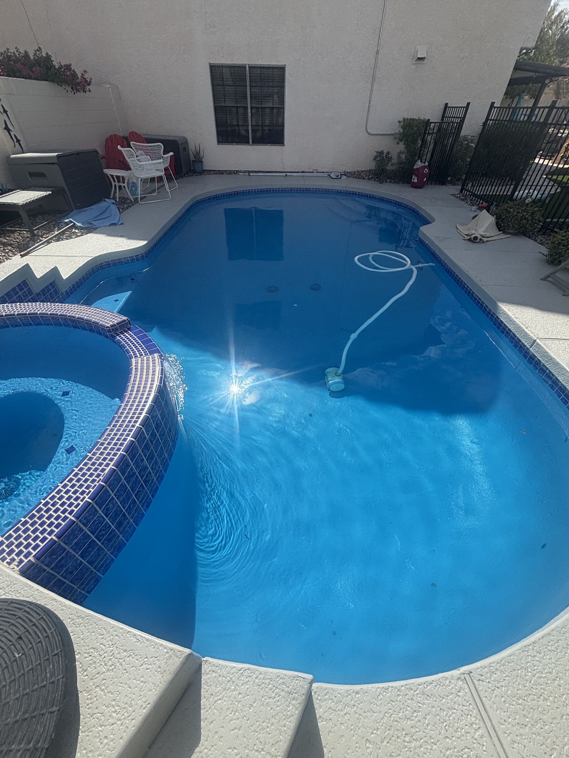Backyard swimming pool with blue water, white deck, and a curved spa in the foreground