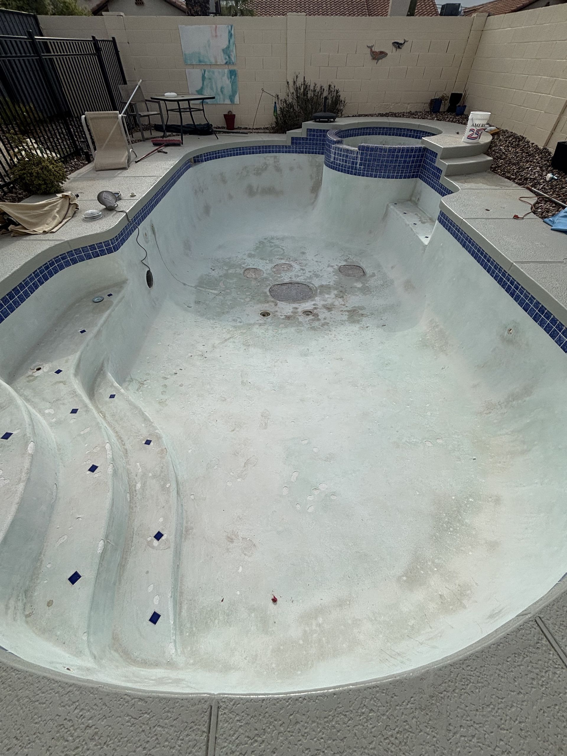 Empty, worn swimming pool with peeling white plaster and blue tile trim in a backyard