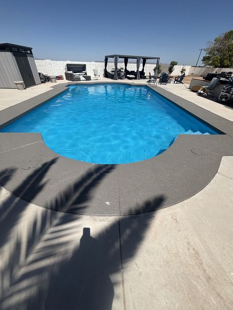 Backyard swimming pool with bright blue water, stone deck, and lounge chairs under a sunny sky