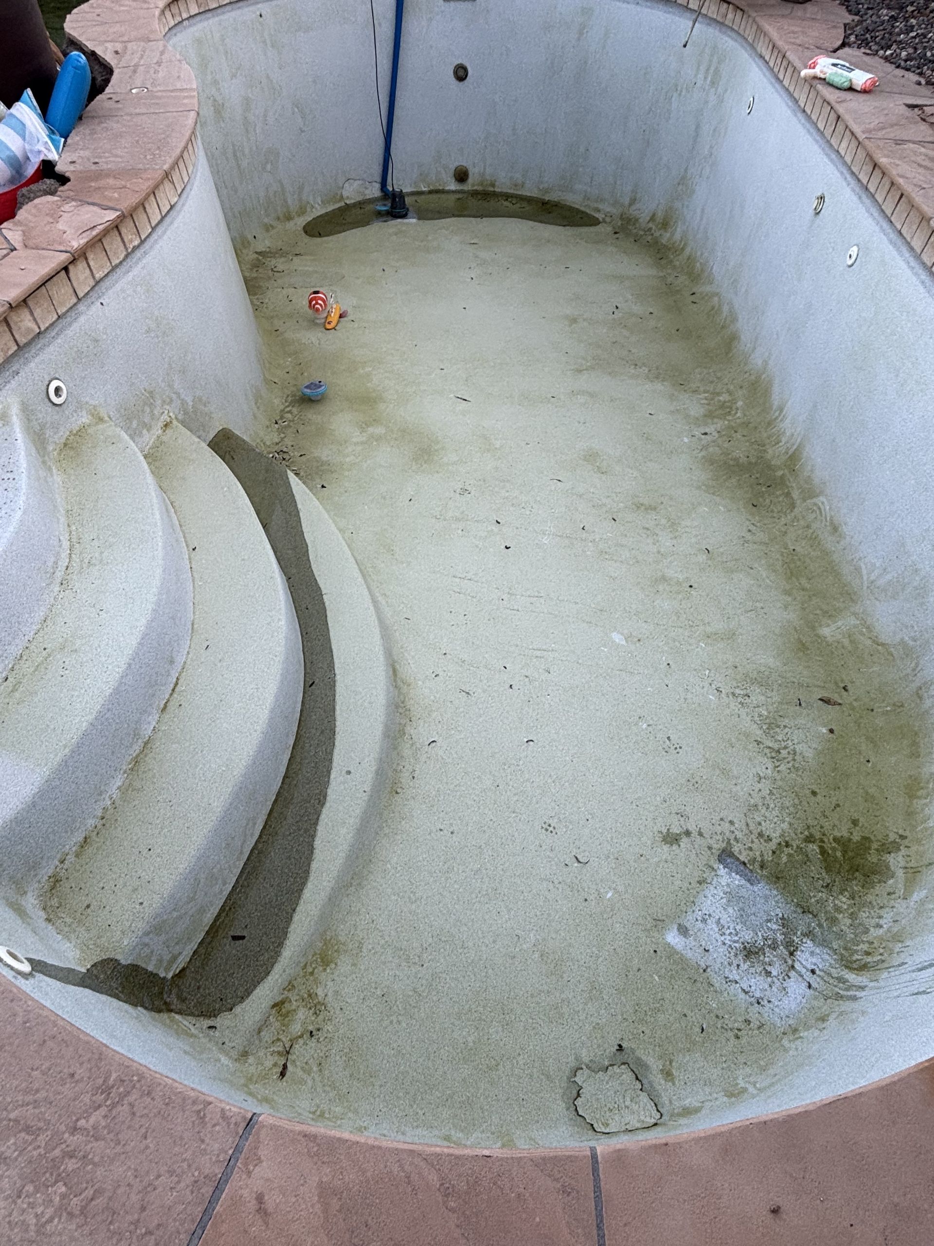 Empty drained swimming pool with stained concrete walls and floor, viewed from above