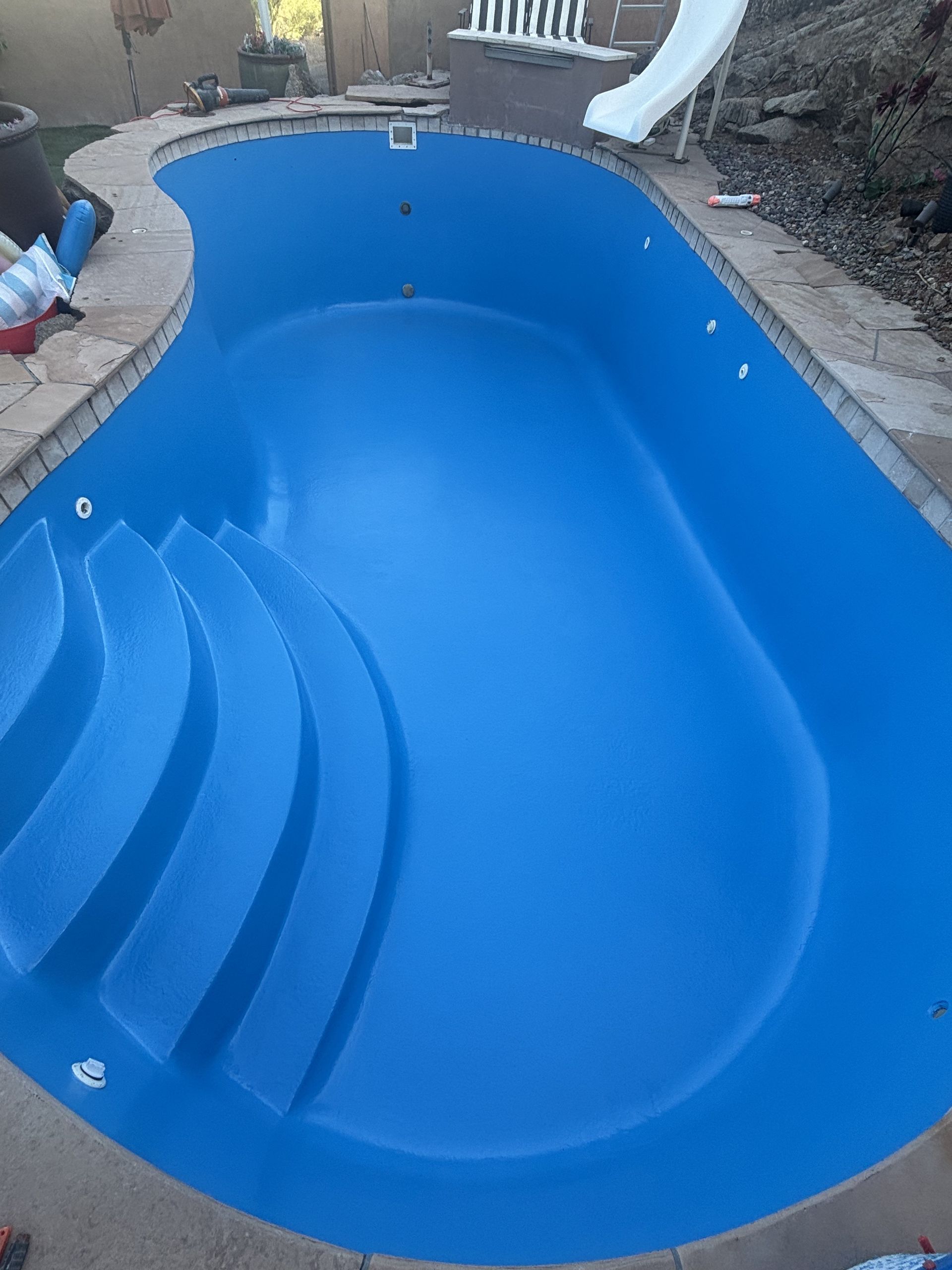 Blue empty backyard swimming pool with built-in steps and a slide