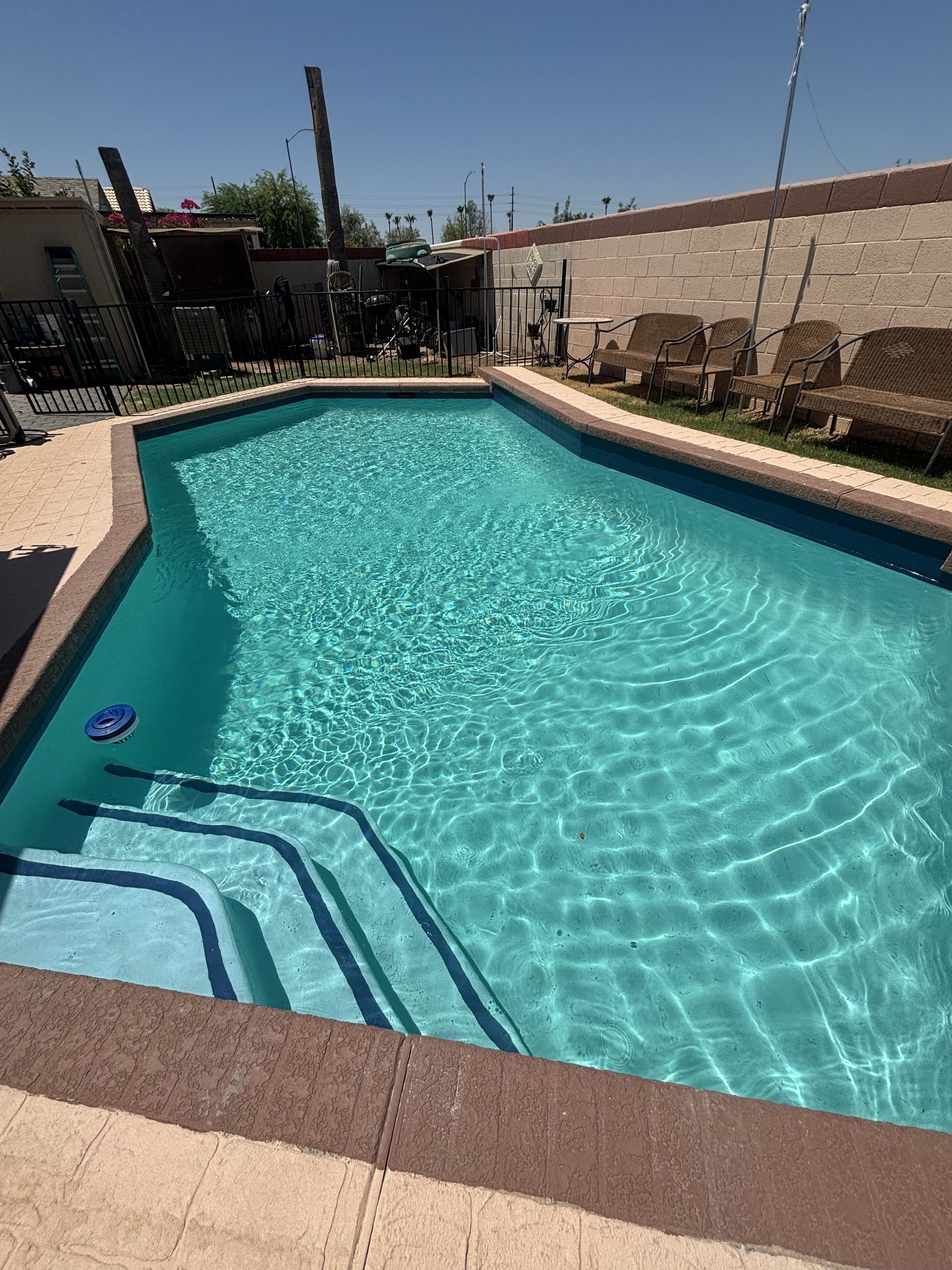 Backyard swimming pool with blue water, concrete deck, and steps at the near end