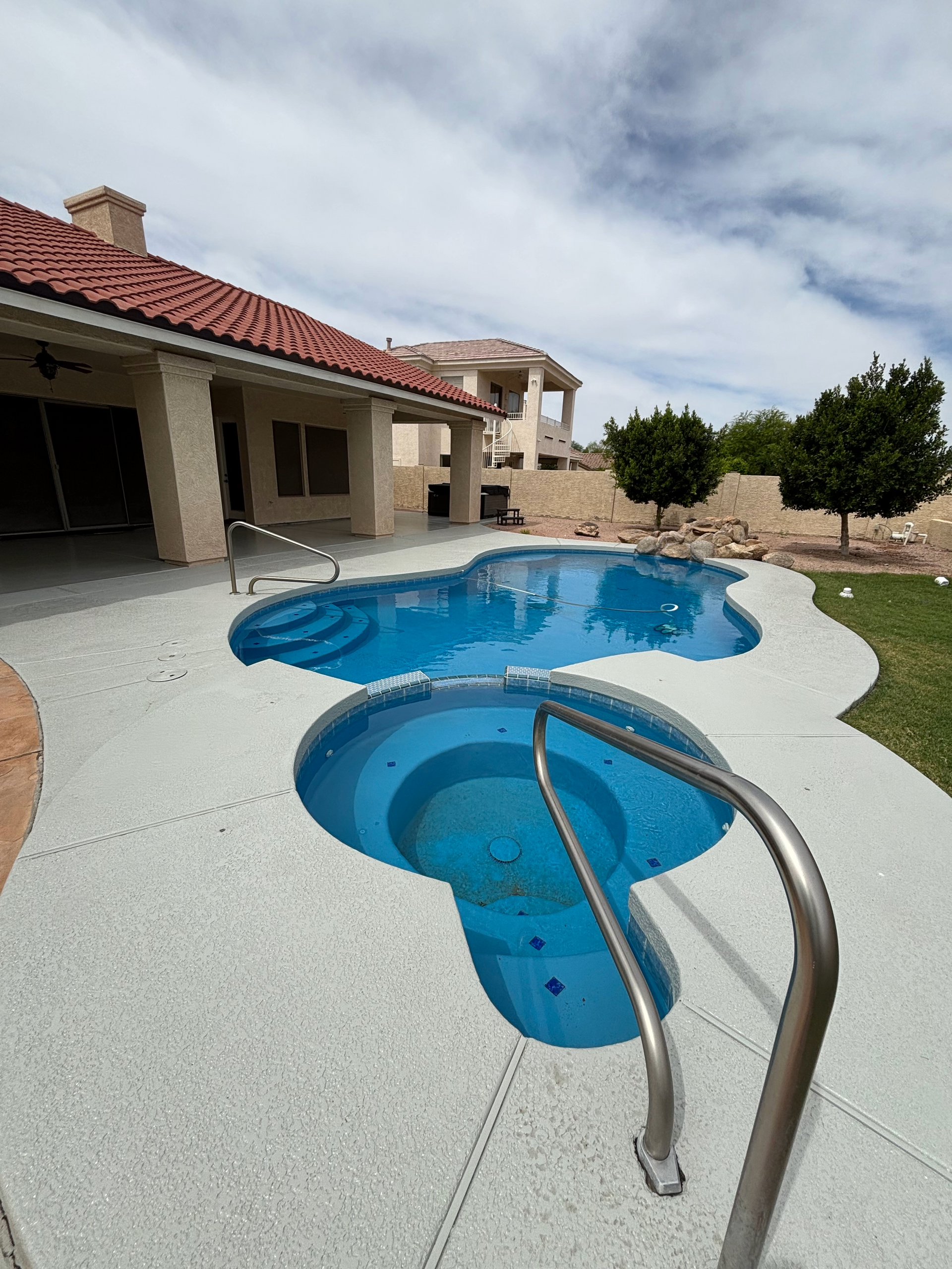 An outdoor backyard with a house, a blue swimming pool, and a smaller, circular spa with a metal safety rail.