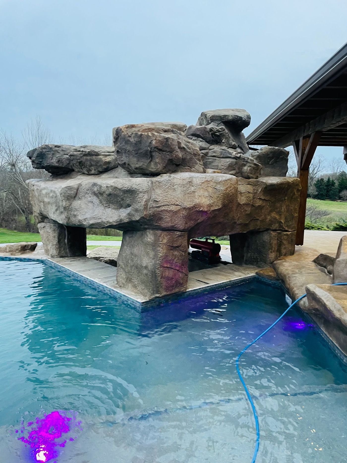 Pool with rock feature and bar, blue water, and overcast sky.