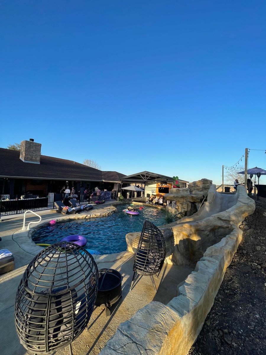 Swimming pool party with people, floats, and sunny sky.