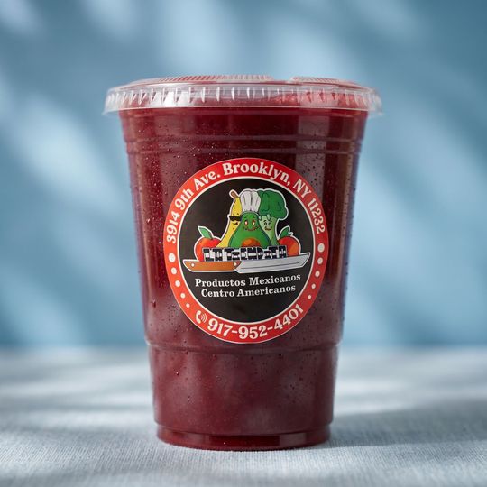 A clear plastic cup of dark red iced drink with a red deli logo on a light blue background