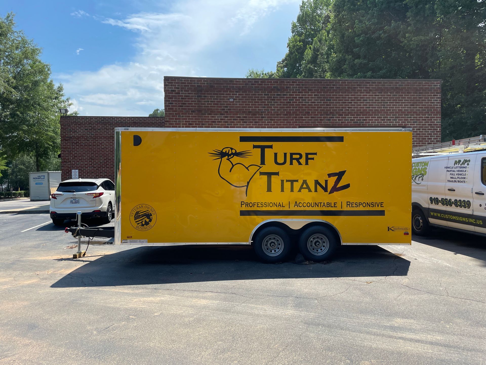 Yellow Turf Titanz trailer parked outside a brick building under a blue sky
