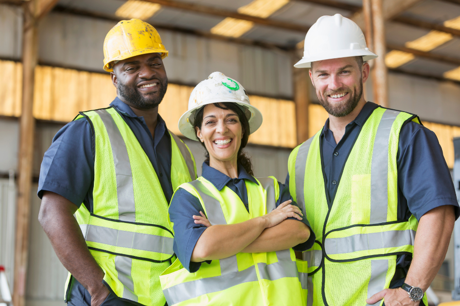 A group of construction workers are posing for a picture in a warehouse.