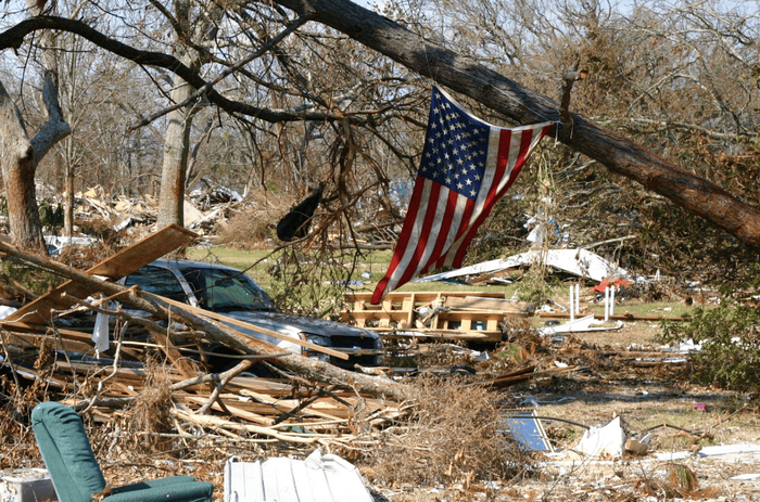 An american flag is hanging from a tree in a damaged area.