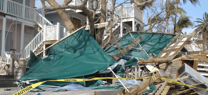 A green tarp is laying on the ground in front of a damaged house.