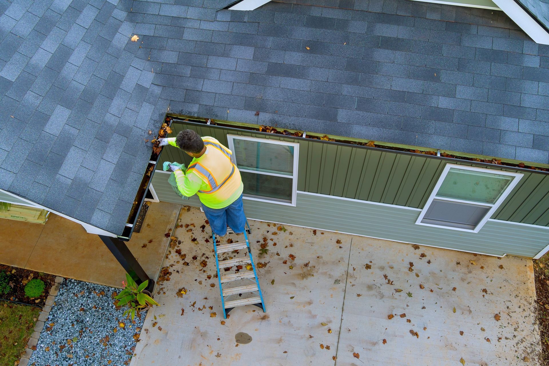 Person on ladder cleaning gutters of a house.