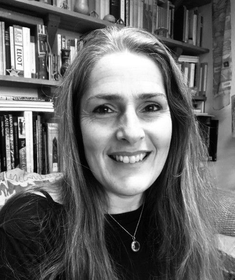 A woman is smiling in a black and white photo in front of a bookshelf.