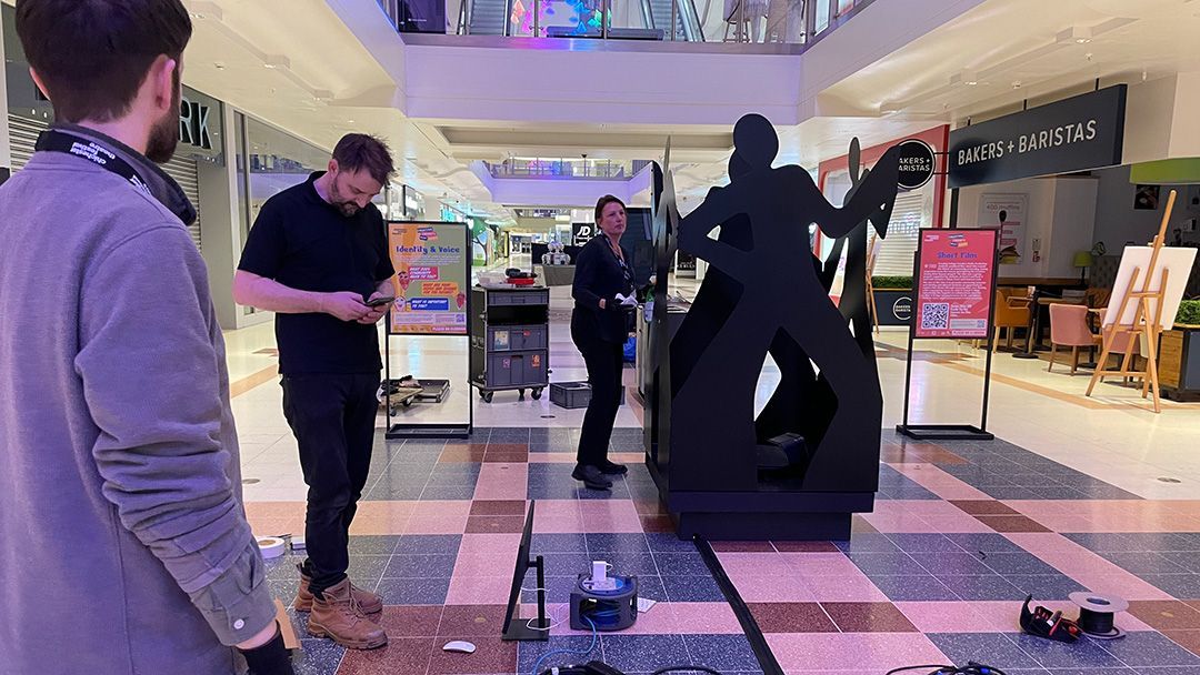 A group of people are standing around a metal sculpture in a mall.