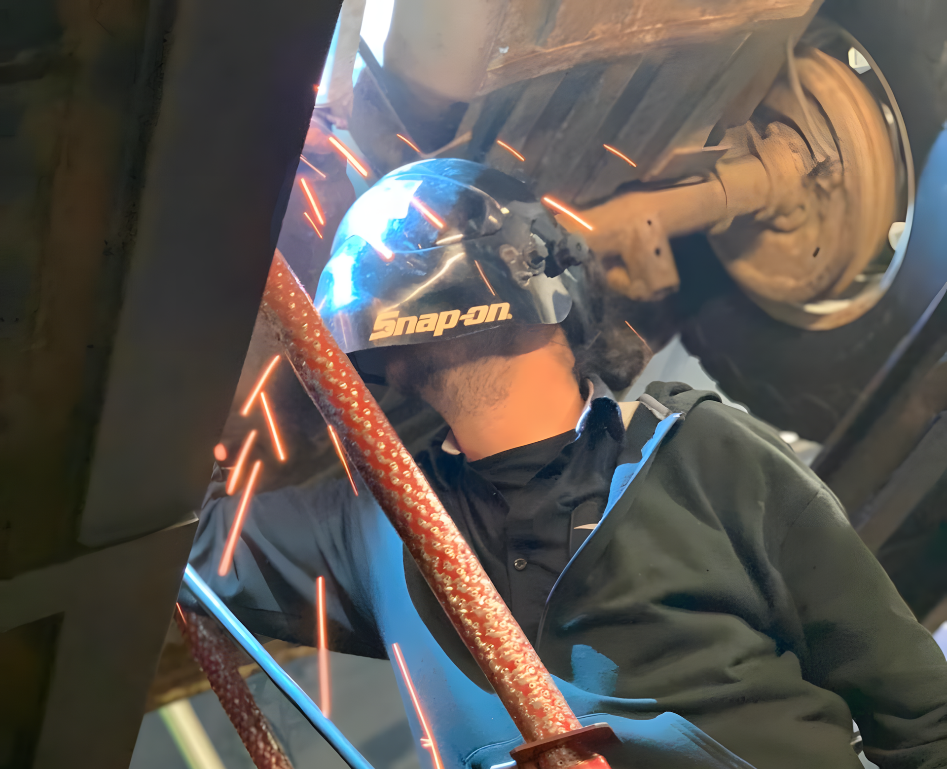 Person welding under a vehicle, wearing a welding helmet. | Total Automotive