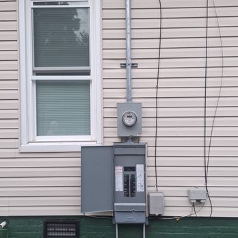 There is a electrical box on the side of a house next to a window.