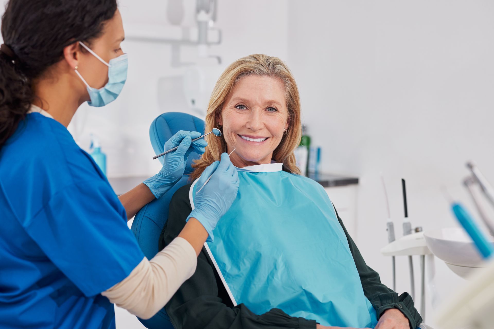 Dental hygienist examining a smiling patient in a clinic, wearing blue gloves and a mask Dental hygienist examining a smiling patient in a clinic, wearing blue gloves and a mask