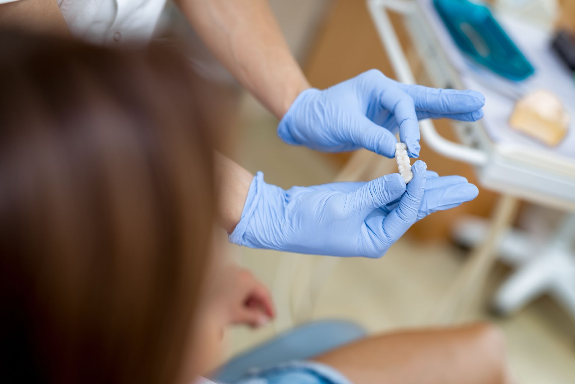 Gloved hands holding a small vial in a medical setting, with a blurred patient in the foreground