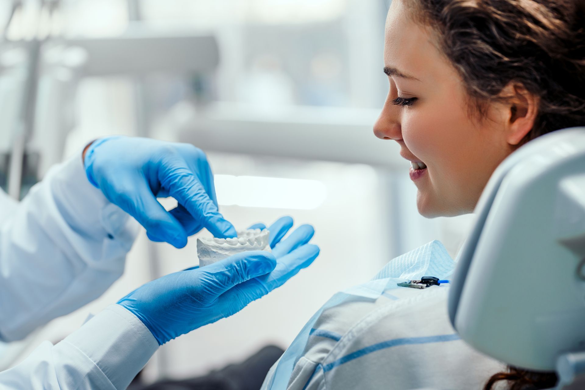 Dental professional in blue gloves examining a patient in a clinic, with the patient smiling and reclined.