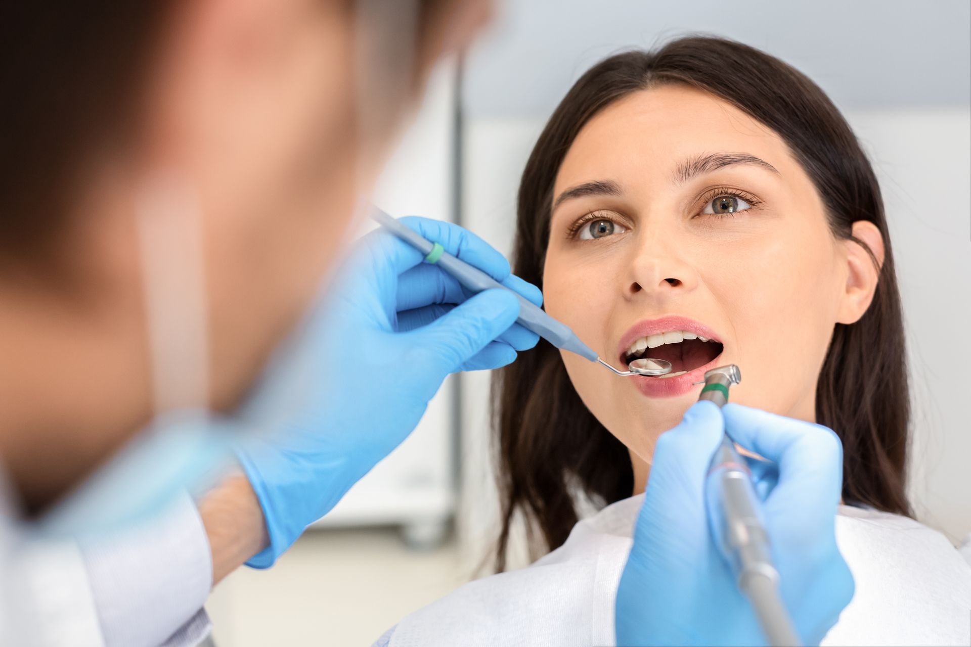Dentist examining a patient’s open mouth with gloved hands and dental tools
