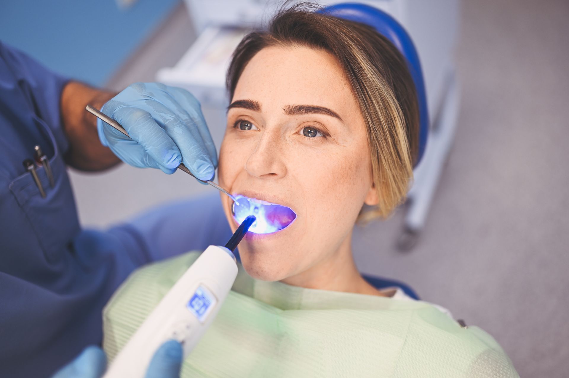 Dentist using a blue curing light on a patient wearing a cheek retractor during a dental procedure